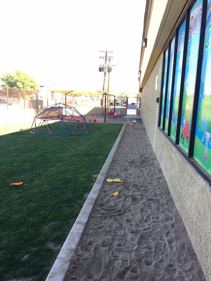 Outdoor playground with a climbing dome, sand area, and building with windows