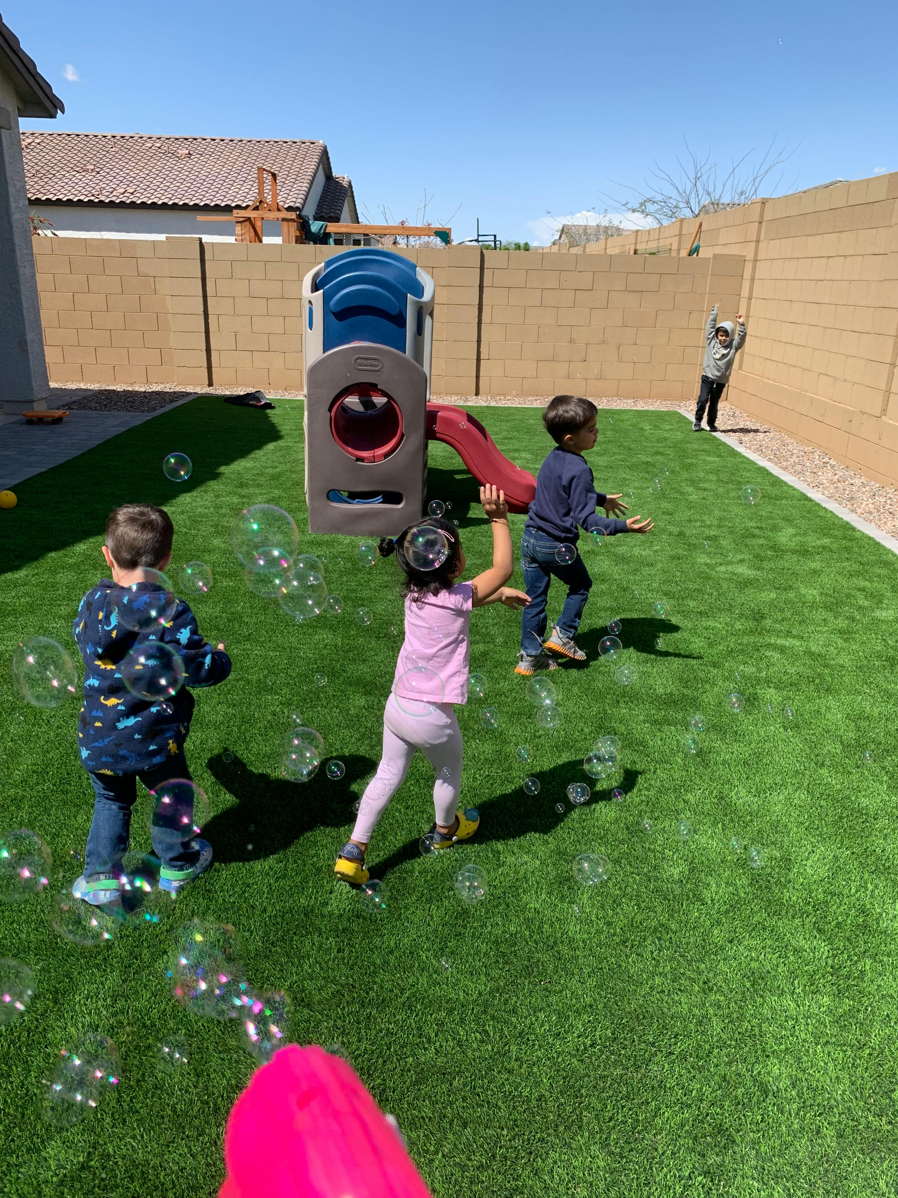 Children playing with bubbles in a grassy backyard
