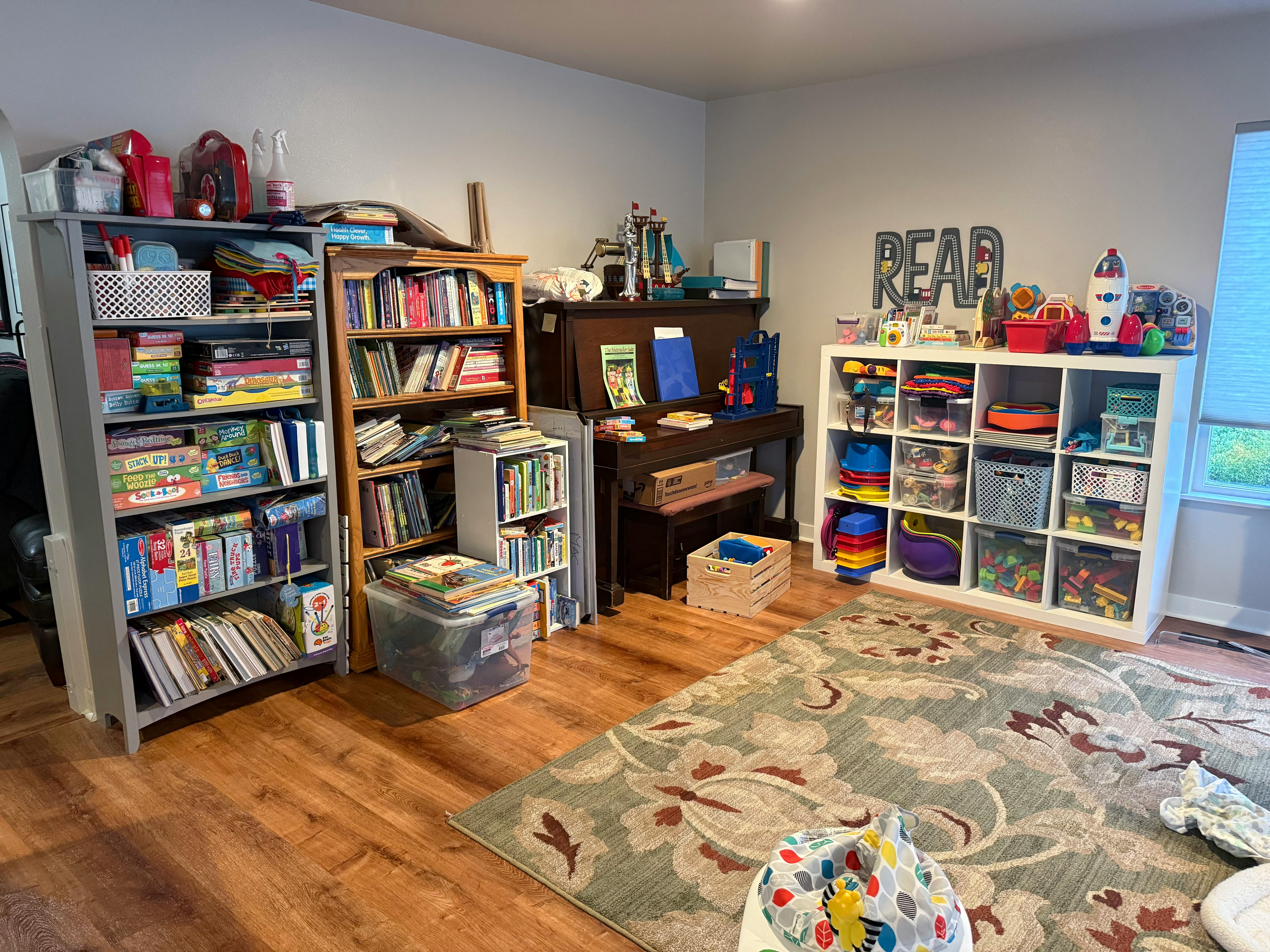 Room with bookshelves, a piano, and a storage unit with toys