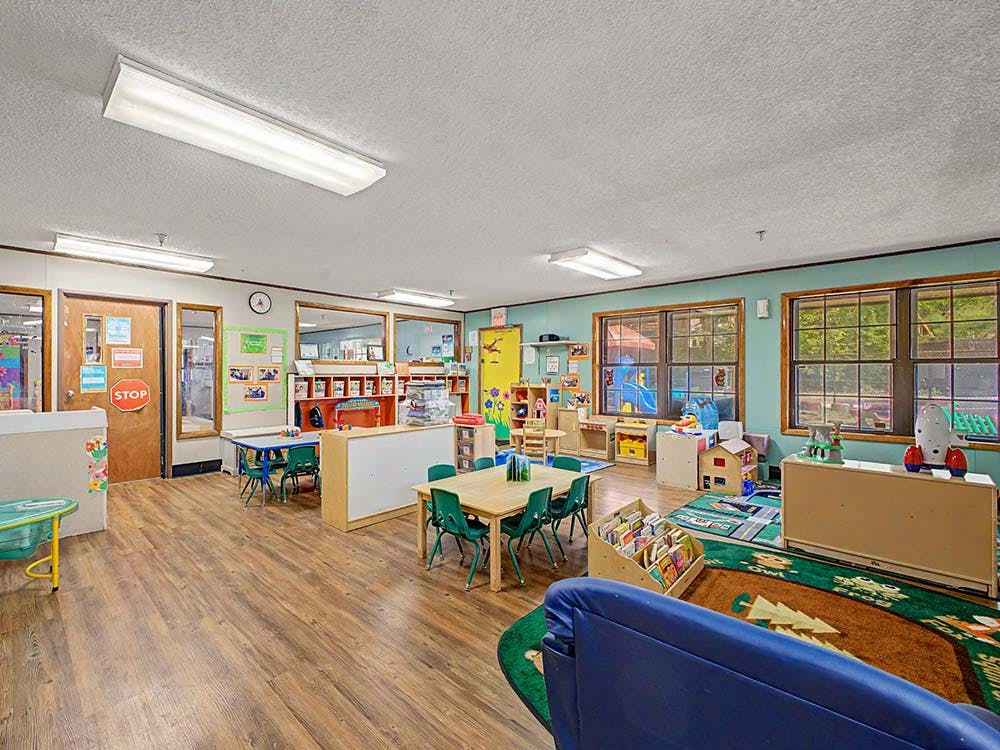 Classroom with small tables and chairs, shelves, and a play area