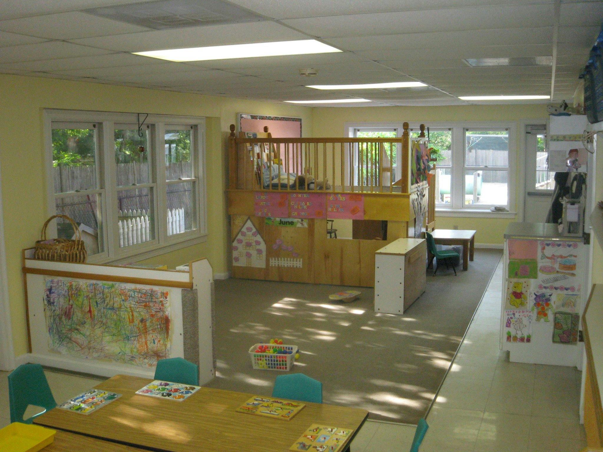 Classroom with a wooden play structure, tables, and windows