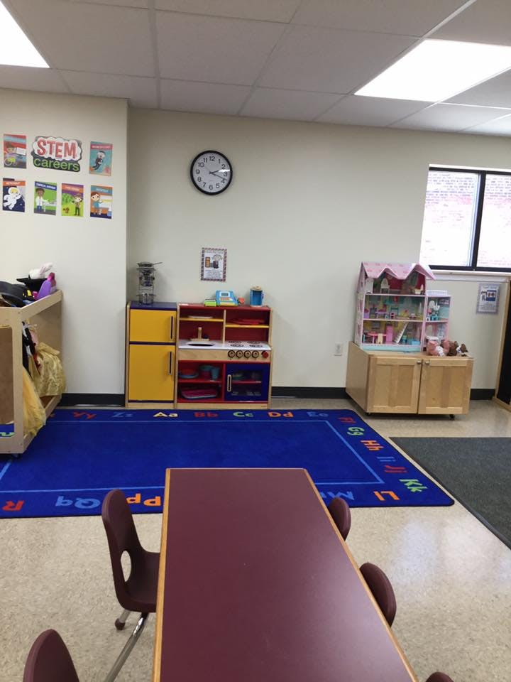 Classroom with a blue rug, play kitchen, and dollhouse