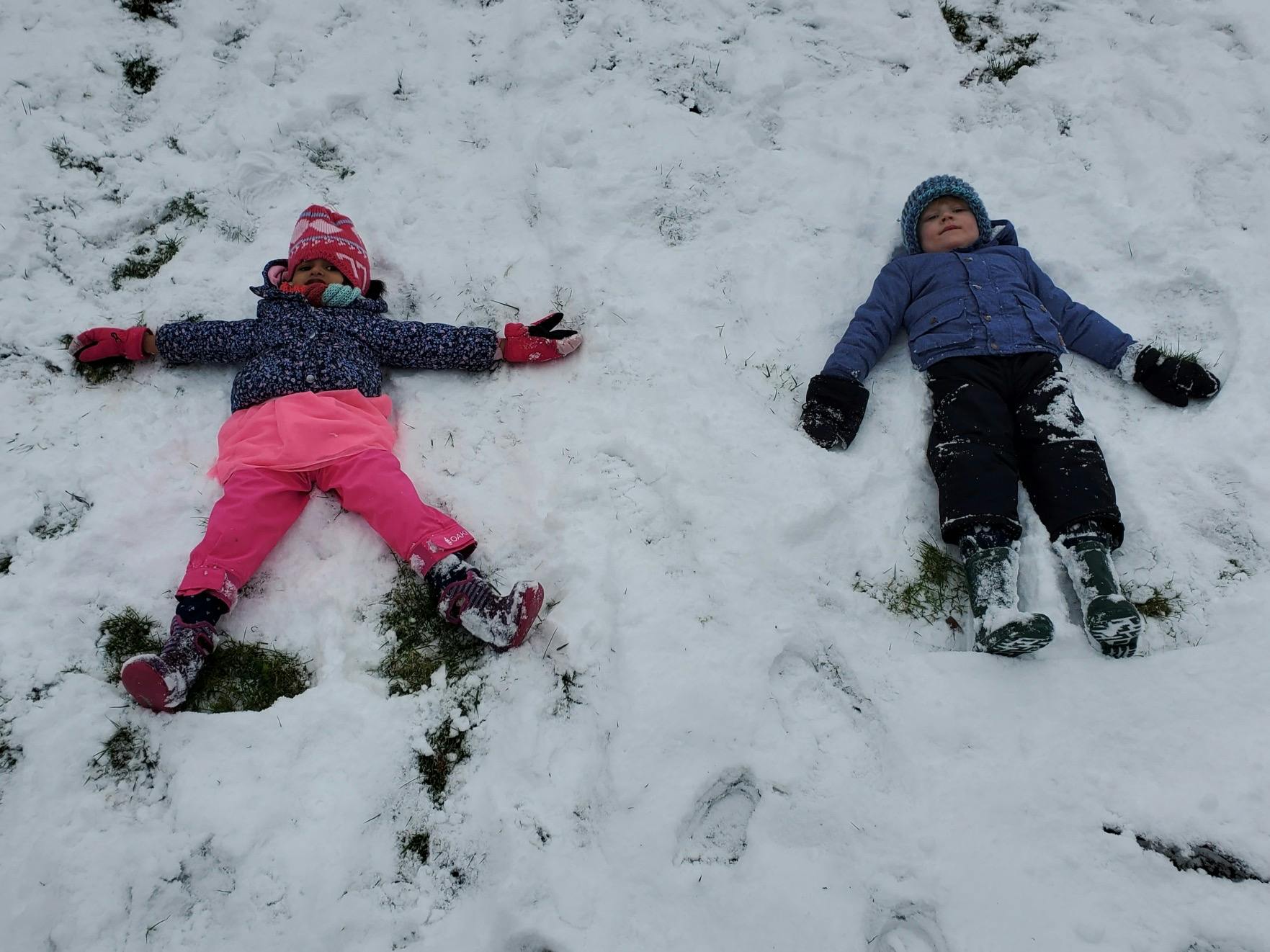 Two children lying in the snow making snow angels