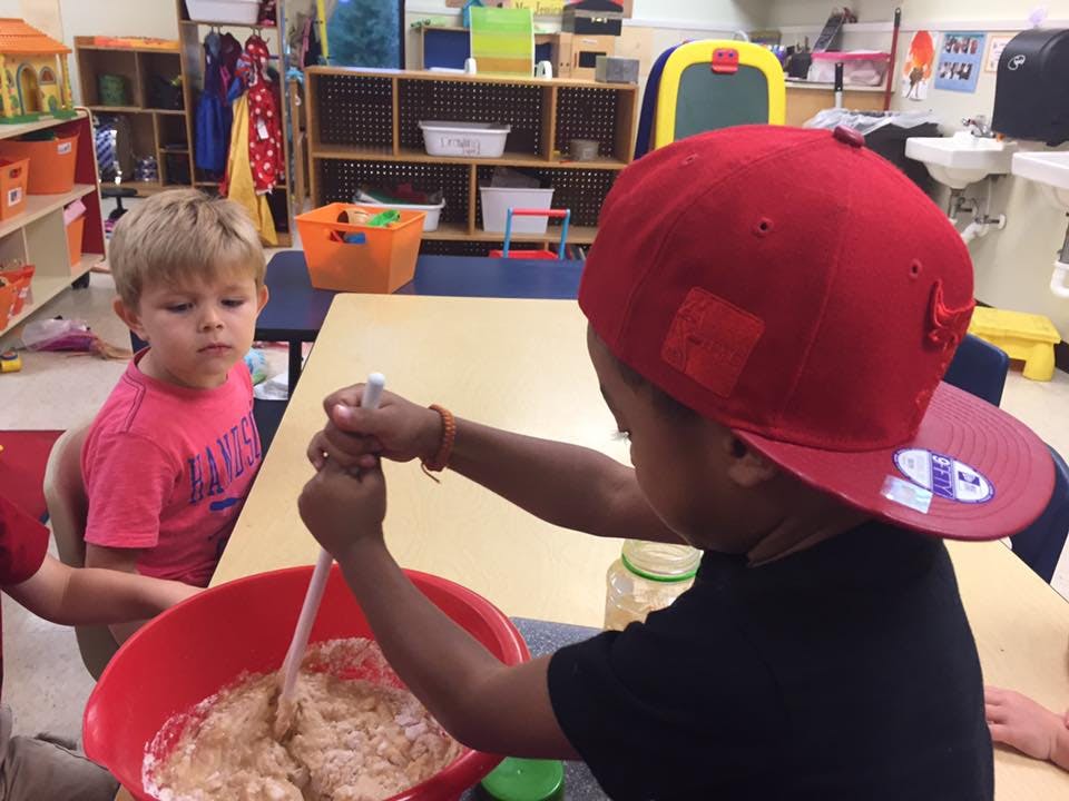 Child in red hat mixing in a bowl, another child watching