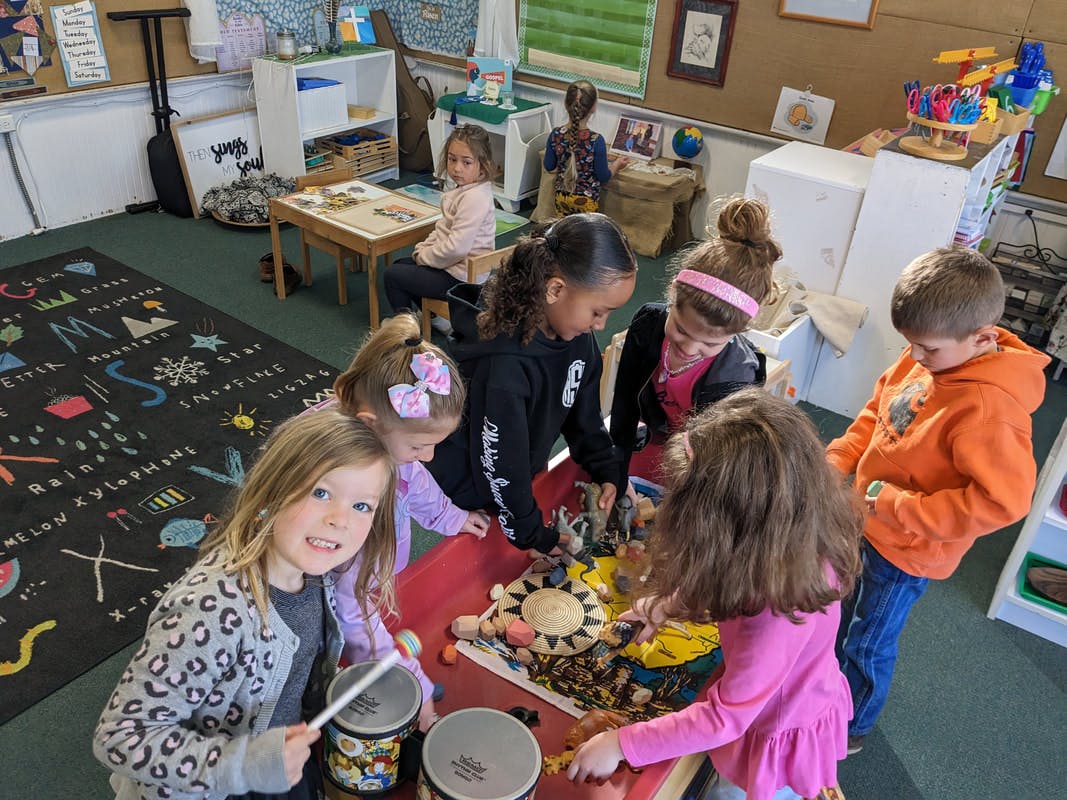 Children gathered around a table with one child playing drums