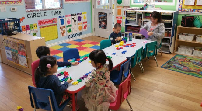 Children and an adult at a table with colorful shapes in a classroom