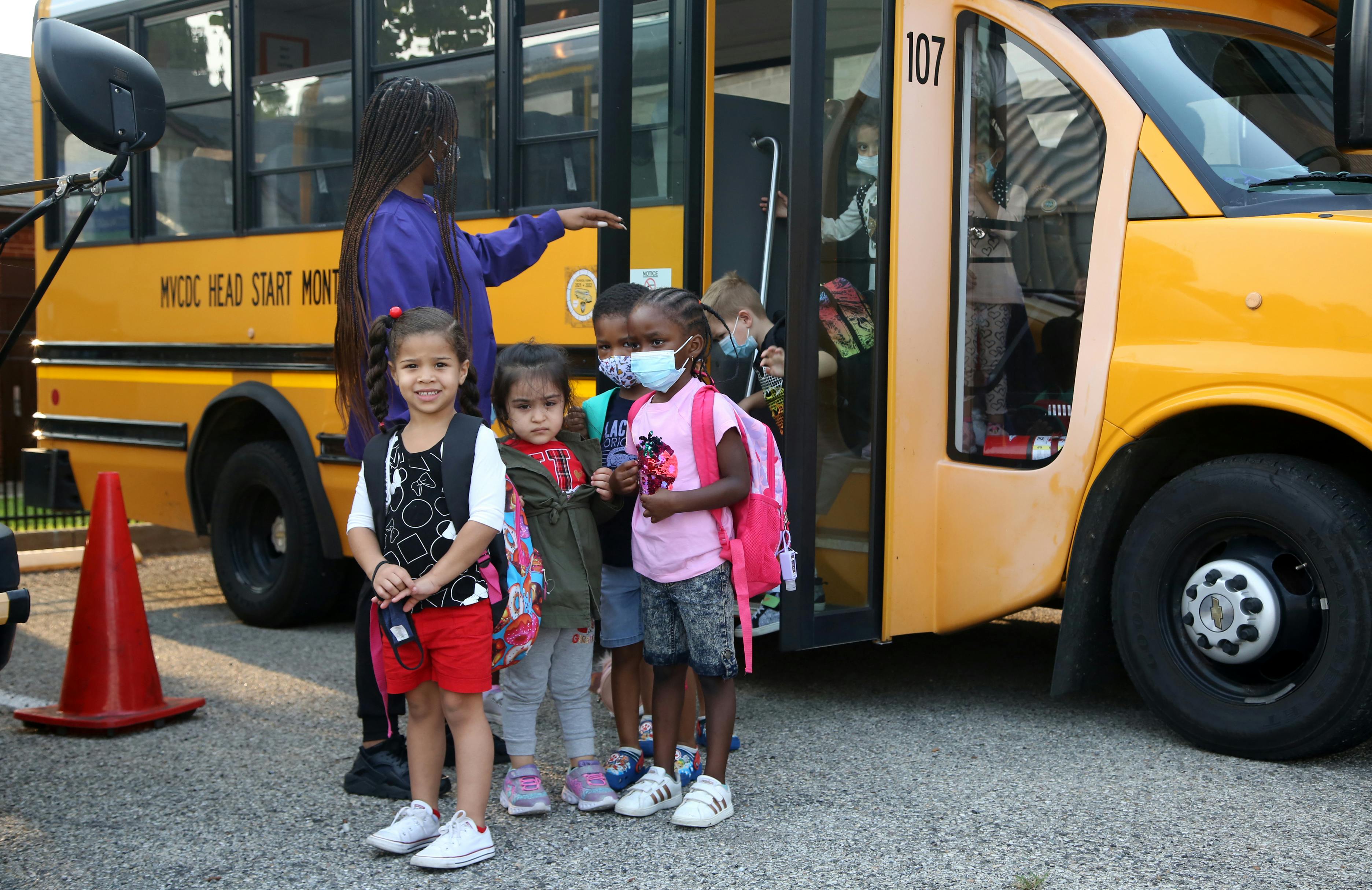 Adult and children standing in front of a school bus