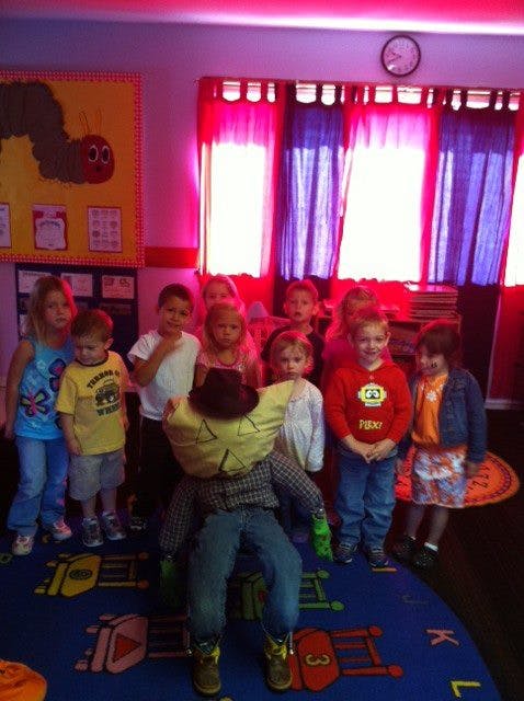 Children standing around a scarecrow in a classroom