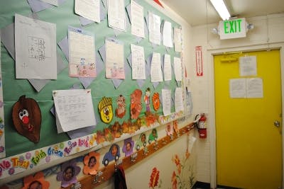 Children's artwork and papers displayed on a classroom wall next to a yellow exit door