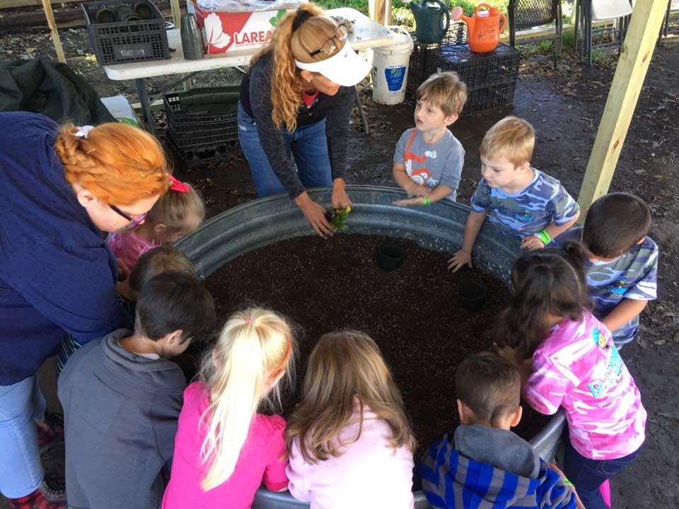 Adults and children gathered around a large metal planter