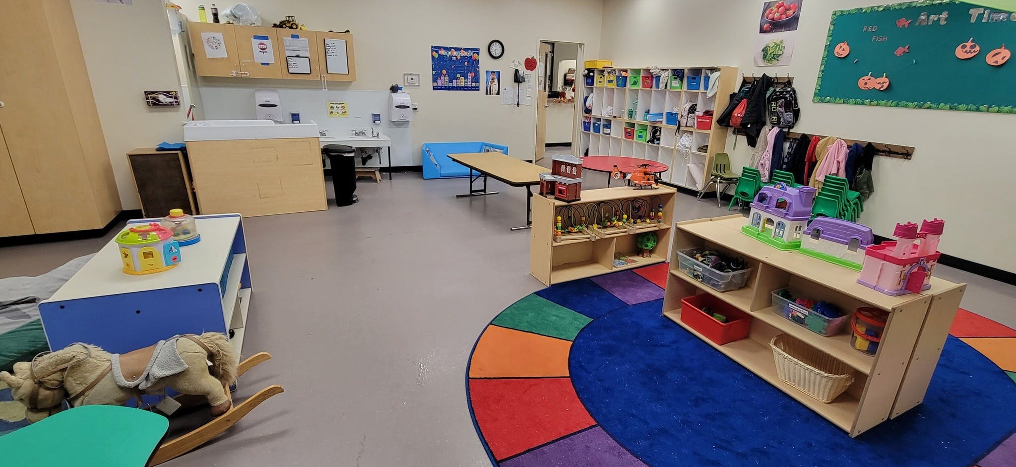Empty classroom with toys, shelves, and a colorful rug