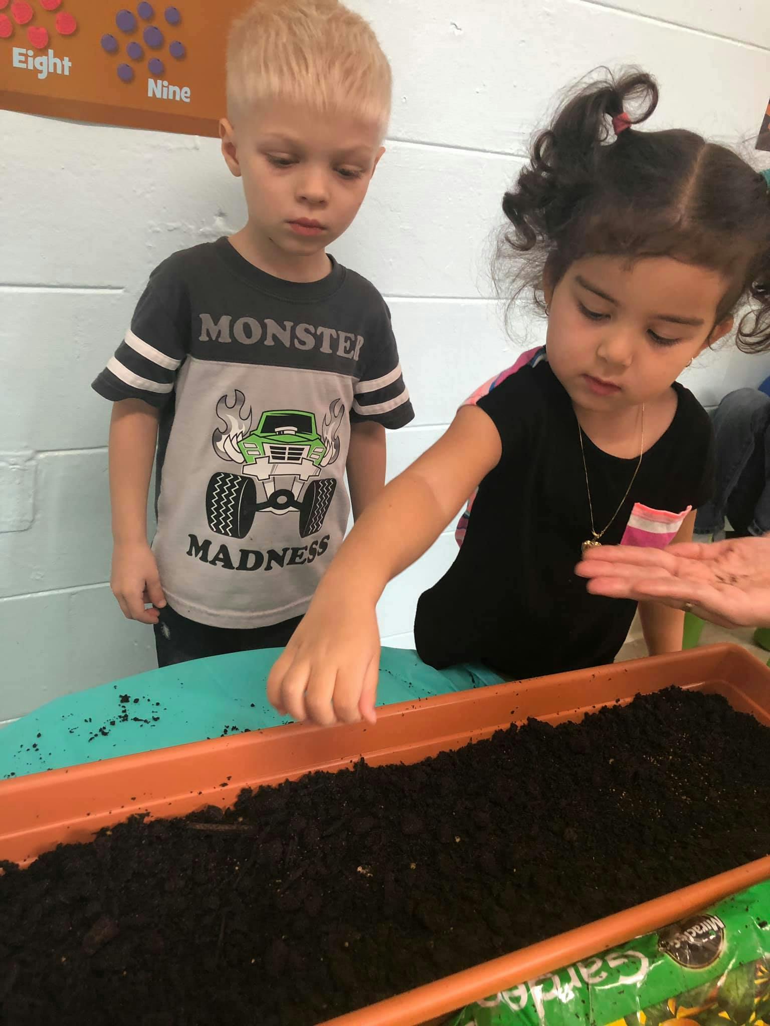 Two children planting seeds in a tray of soil in a classroom