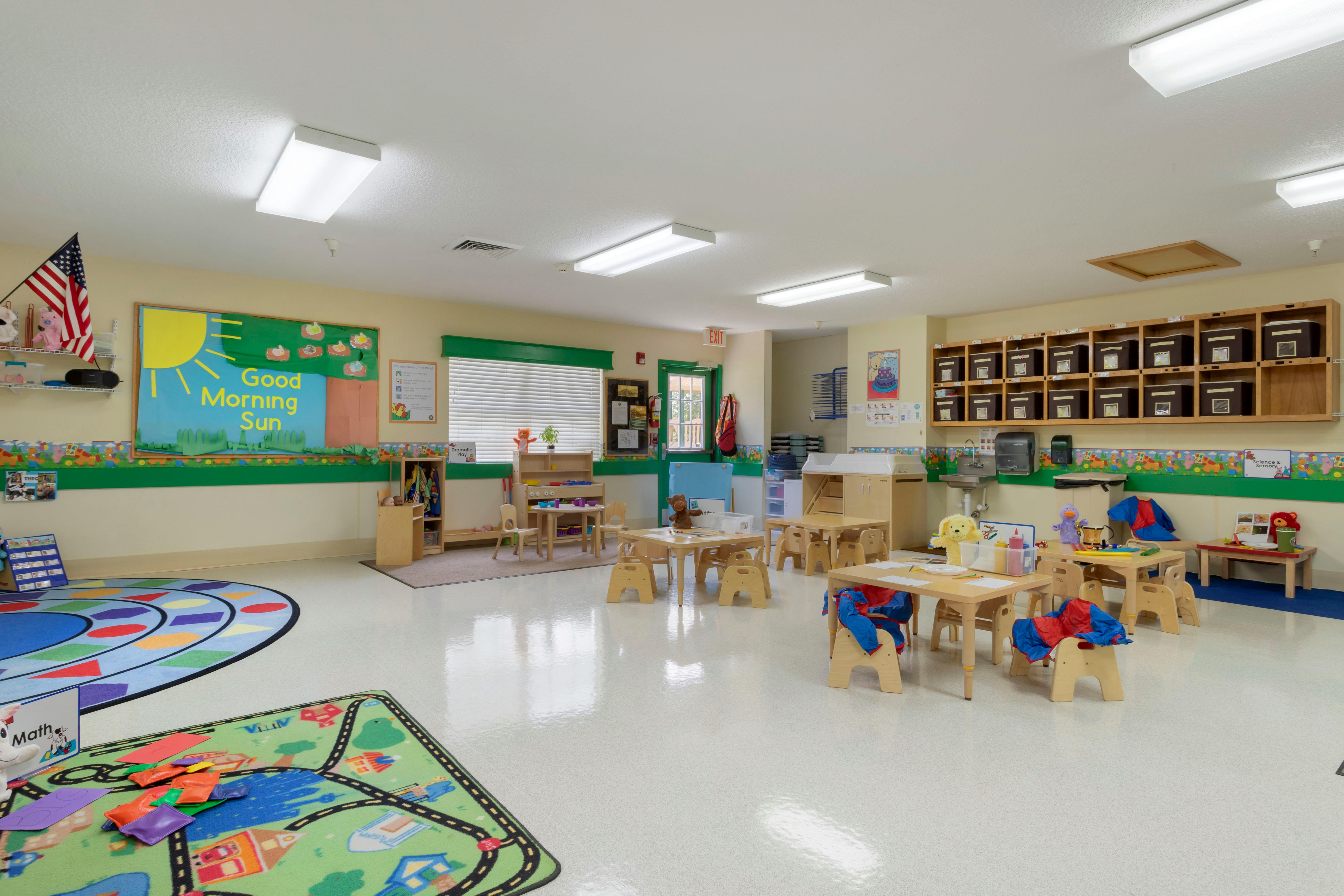 Empty classroom with small tables and chairs, colorful rugs, and learning displays