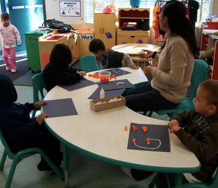 Adult and children doing crafts at a table in a classroom