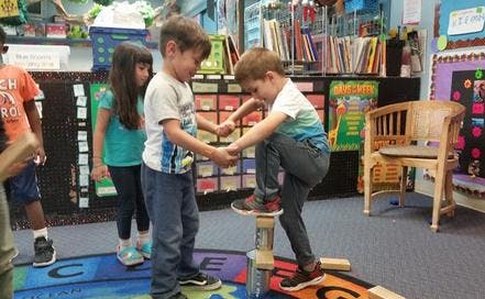 Two children holding hands, one standing on a block structure