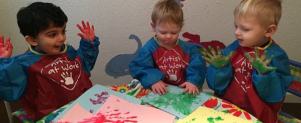 Three children finger painting in smocks