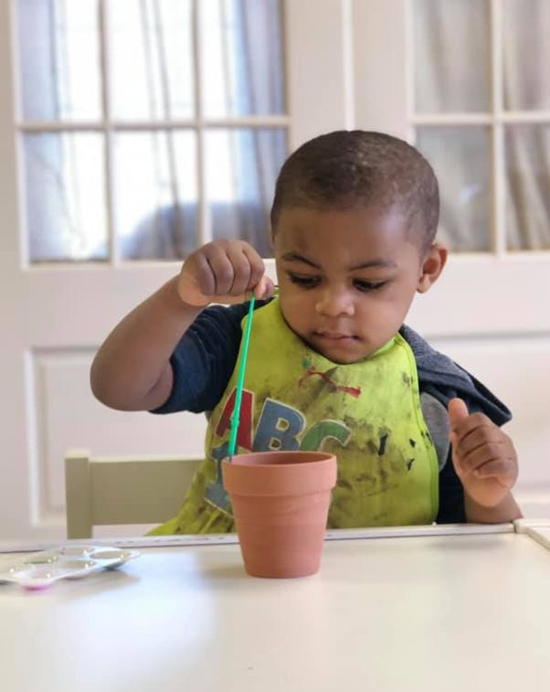 Child in a high chair playing with a green string and a small terracotta pot