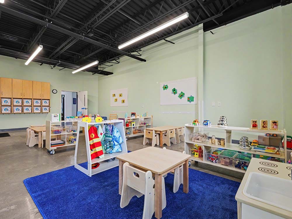 Classroom with small tables, chairs, toy shelves, and dress-up clothes
