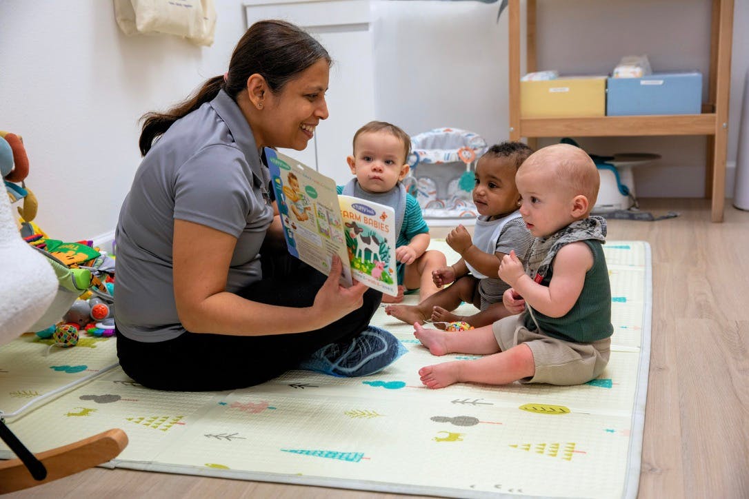 Person reading to three babies on a mat in a classroom