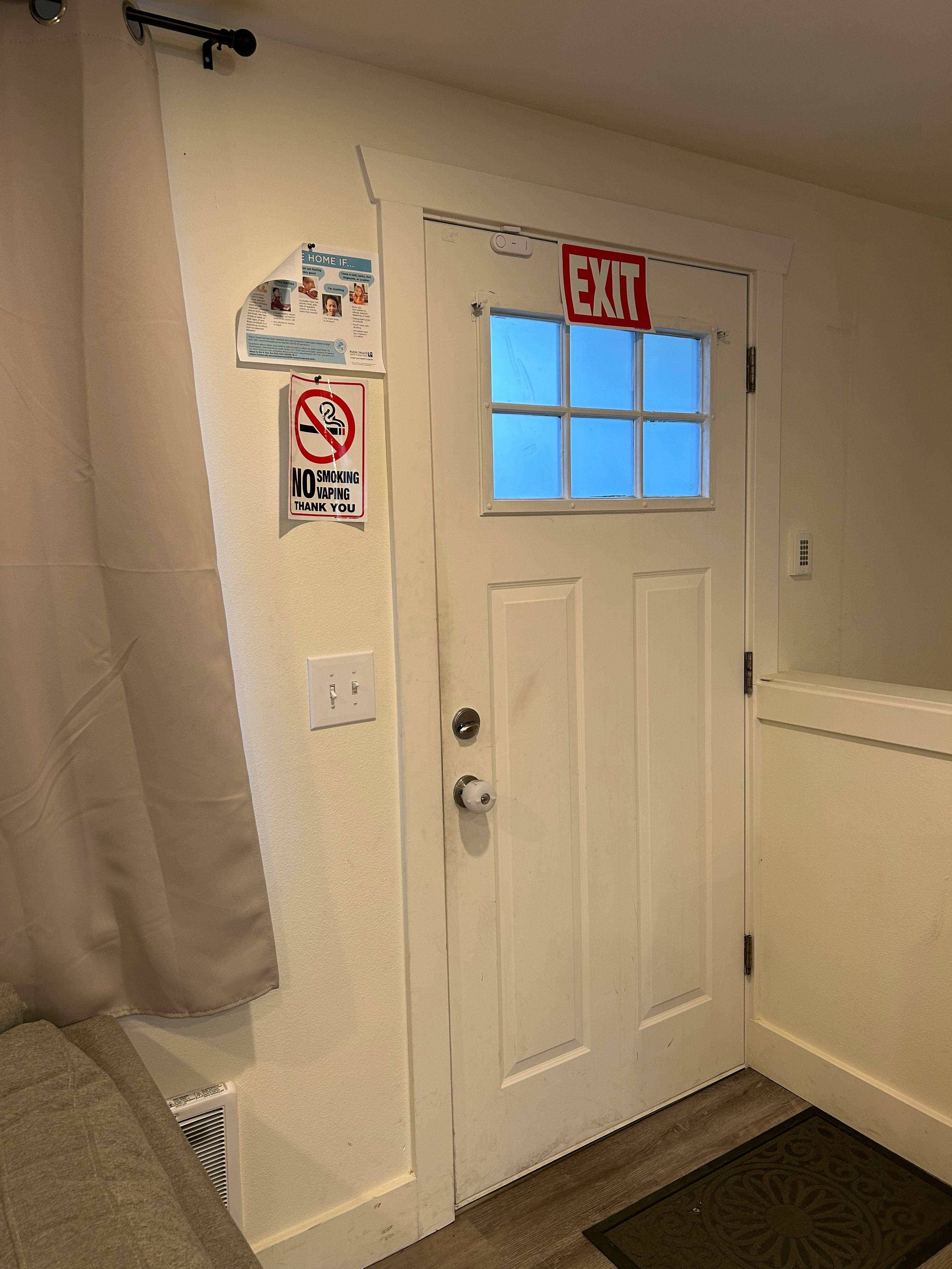White door with an exit sign above a window and a no smoking sign on the wall