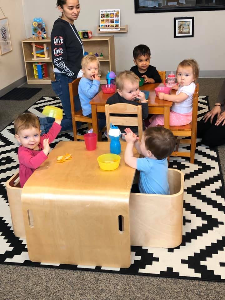 Adult standing near children seated at tables in a classroom