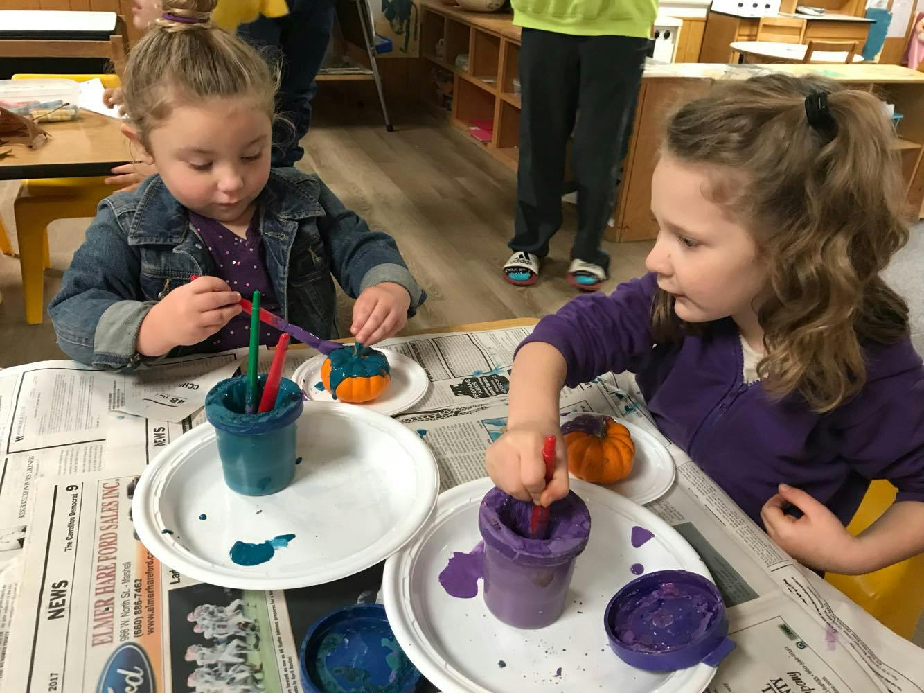 Two children painting small pumpkins at a table