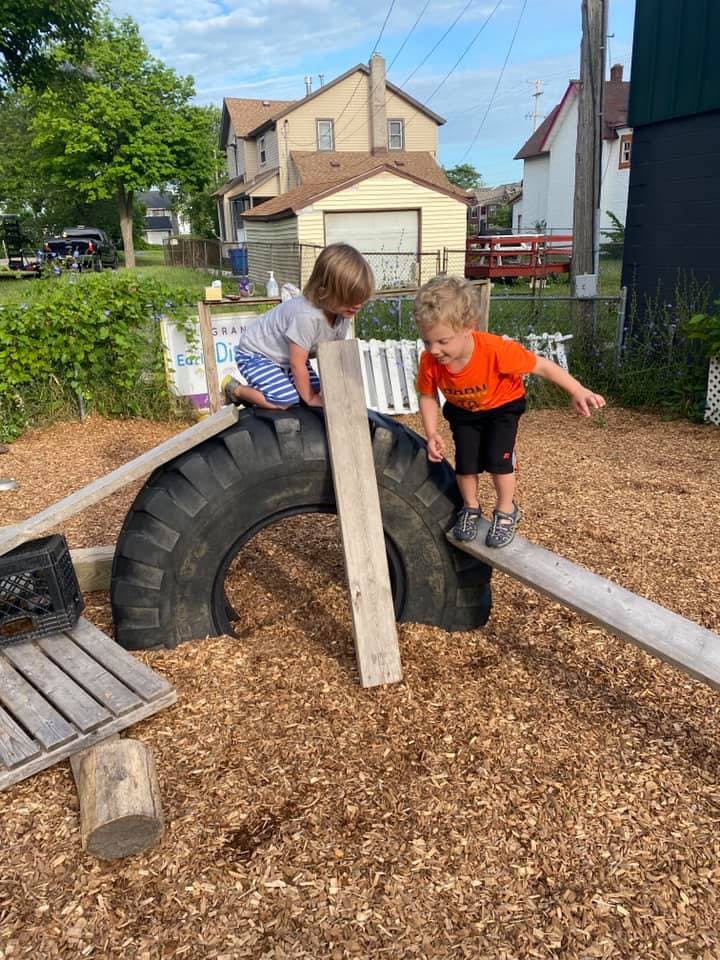 Two children playing on a tire and wooden planks