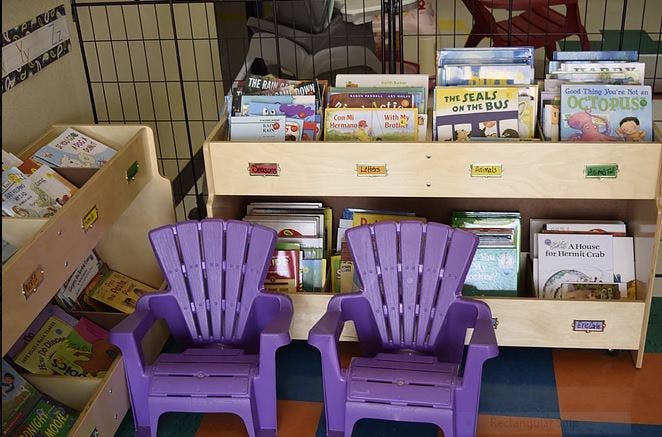 Two purple chairs in front of a bookshelf filled with children's books