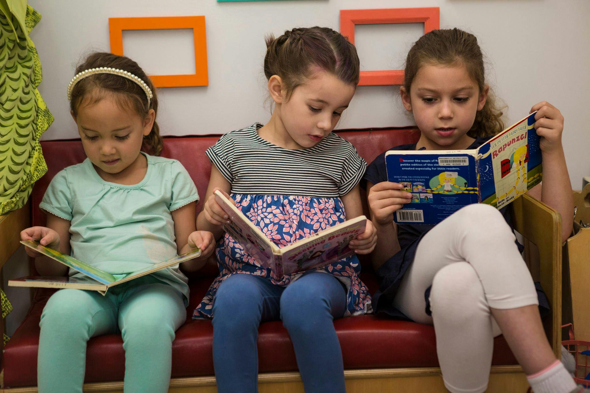 Three children sitting on a bench reading books