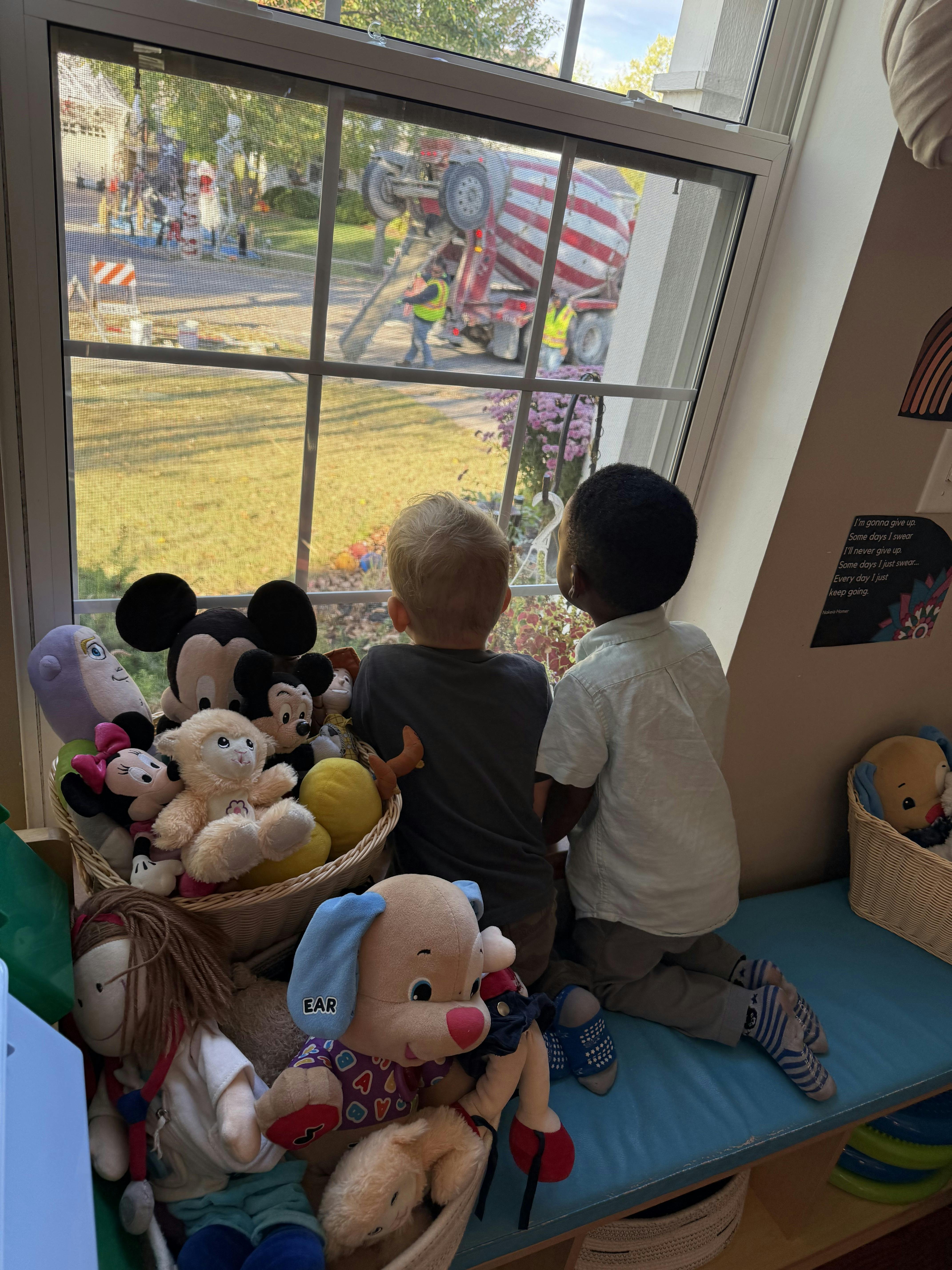 Two children looking out a window at a cement mixer