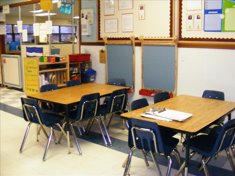 Empty classroom with two tables and chairs, shelves, and chalkboards