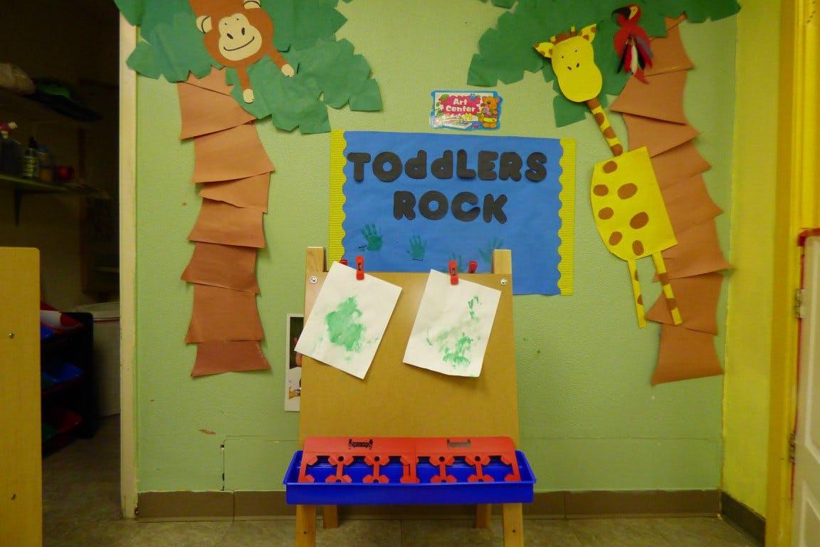 Easel with children's drawings in a classroom with "TODDLERS ROCK" sign