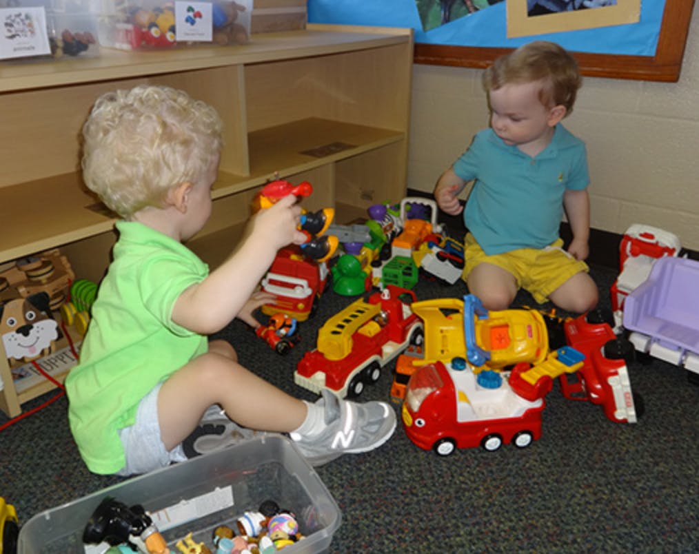 Two children playing with toy trucks and cars on the floor