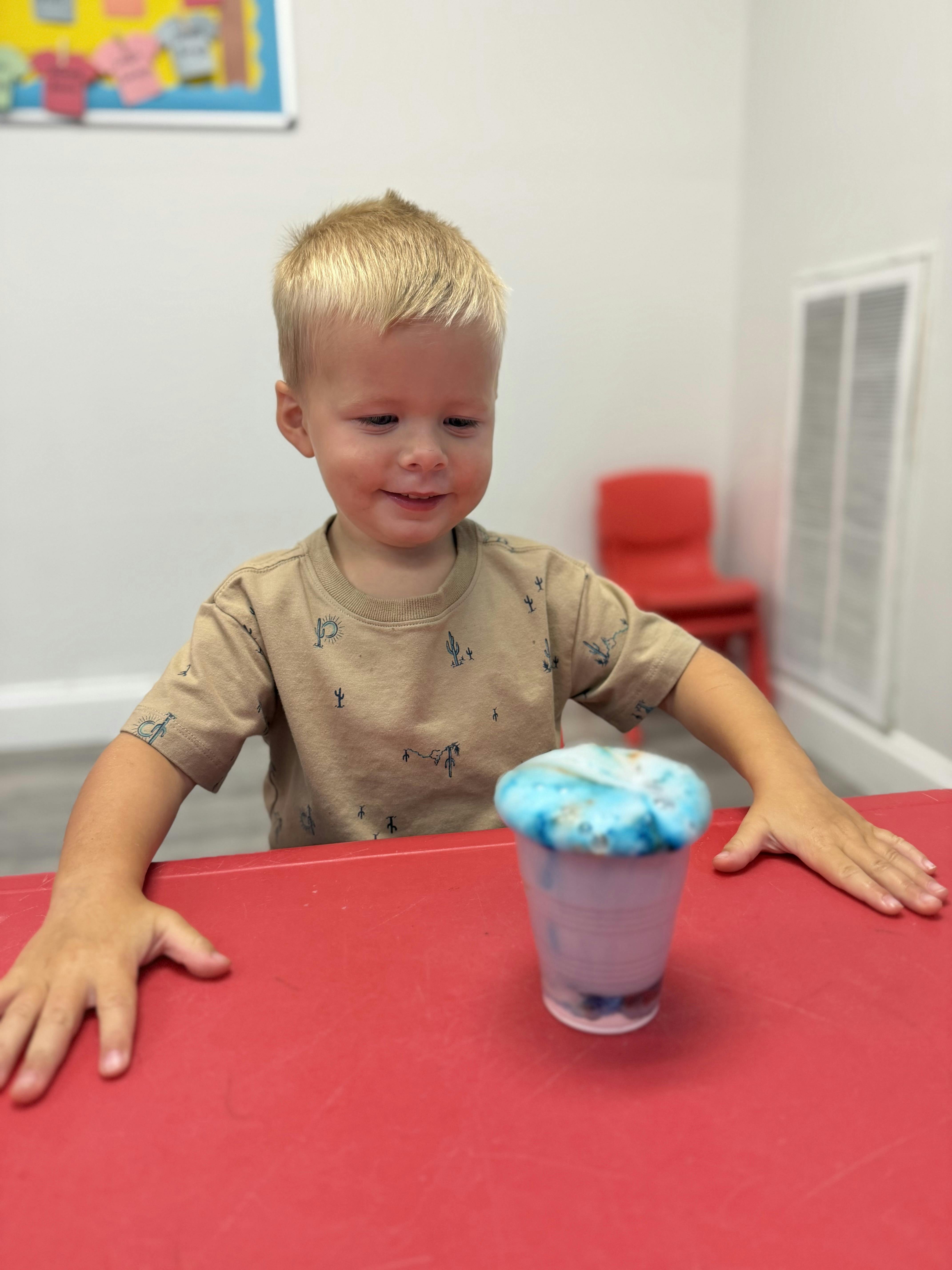 Child sitting at a table with a plastic cup containing a bubbly blue substance