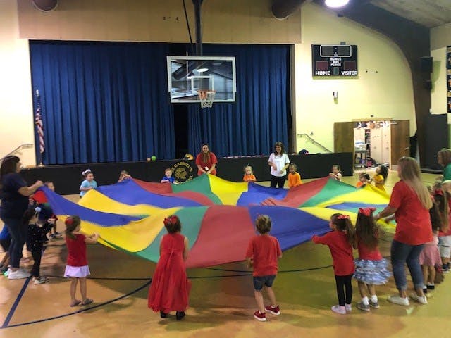 Adults and children playing with a colorful parachute in a gymnasium