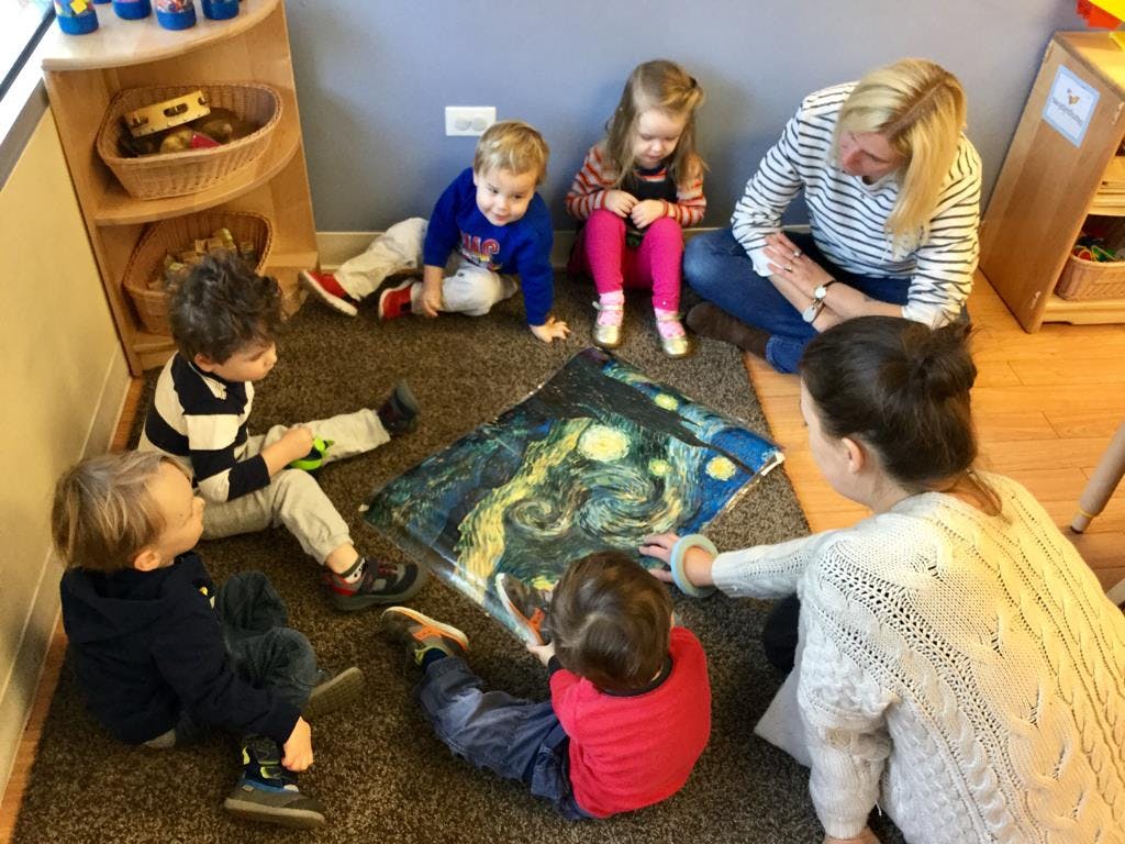 Adults and children sitting on a rug looking at a large picture