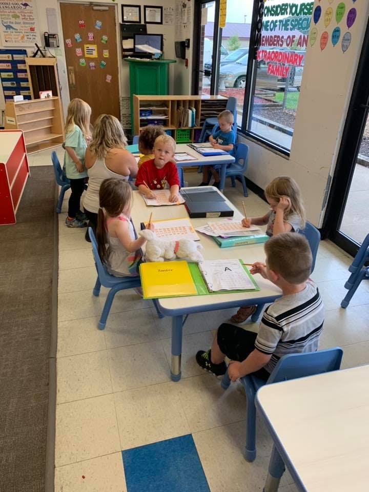 Adult and children sitting at tables in a classroom