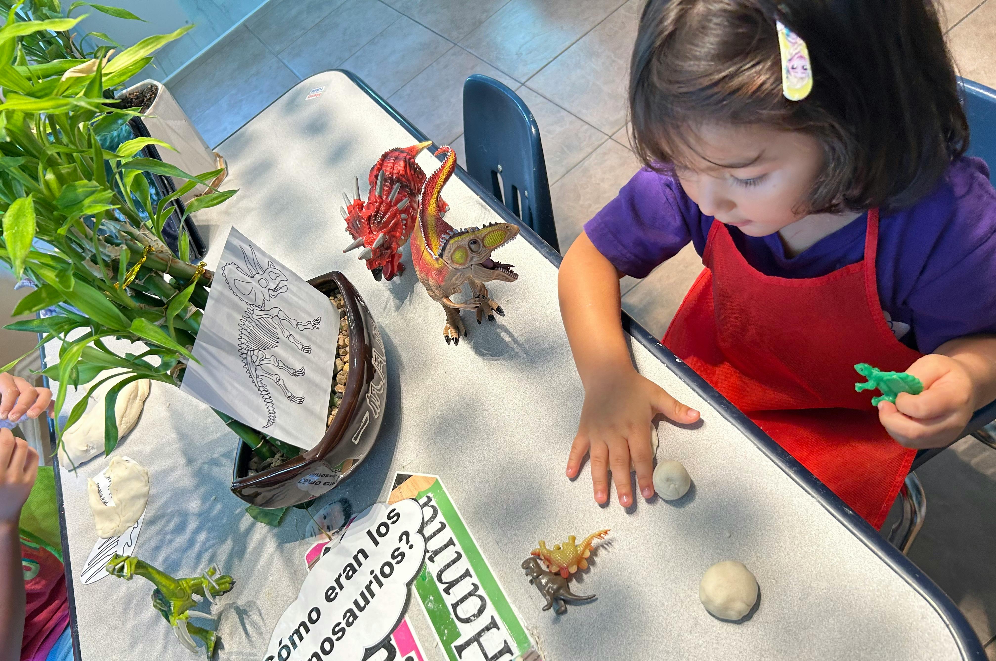 Child playing with dinosaur toys and clay on a table