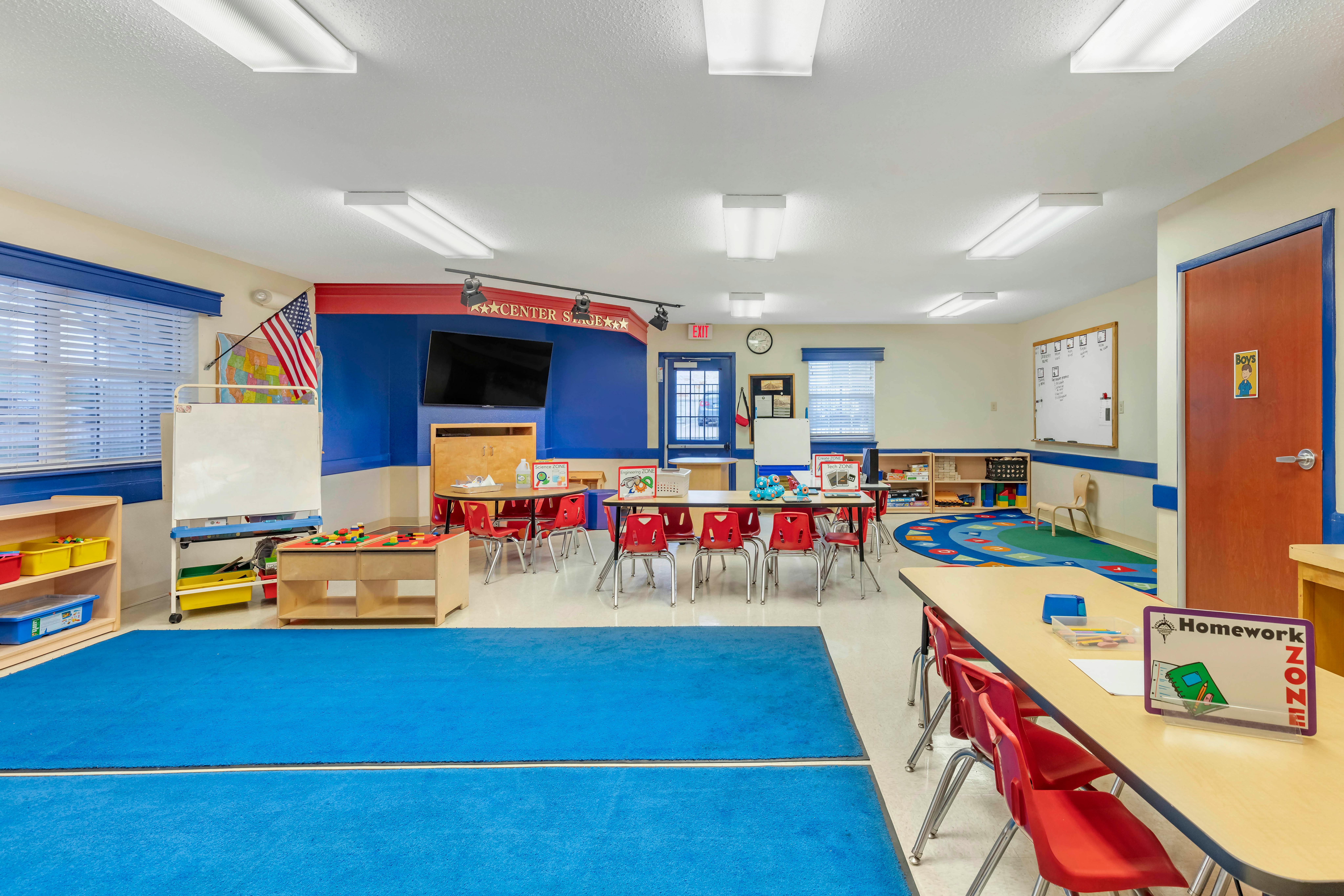 Classroom with small tables and red chairs, blue accent wall, and blue rugs