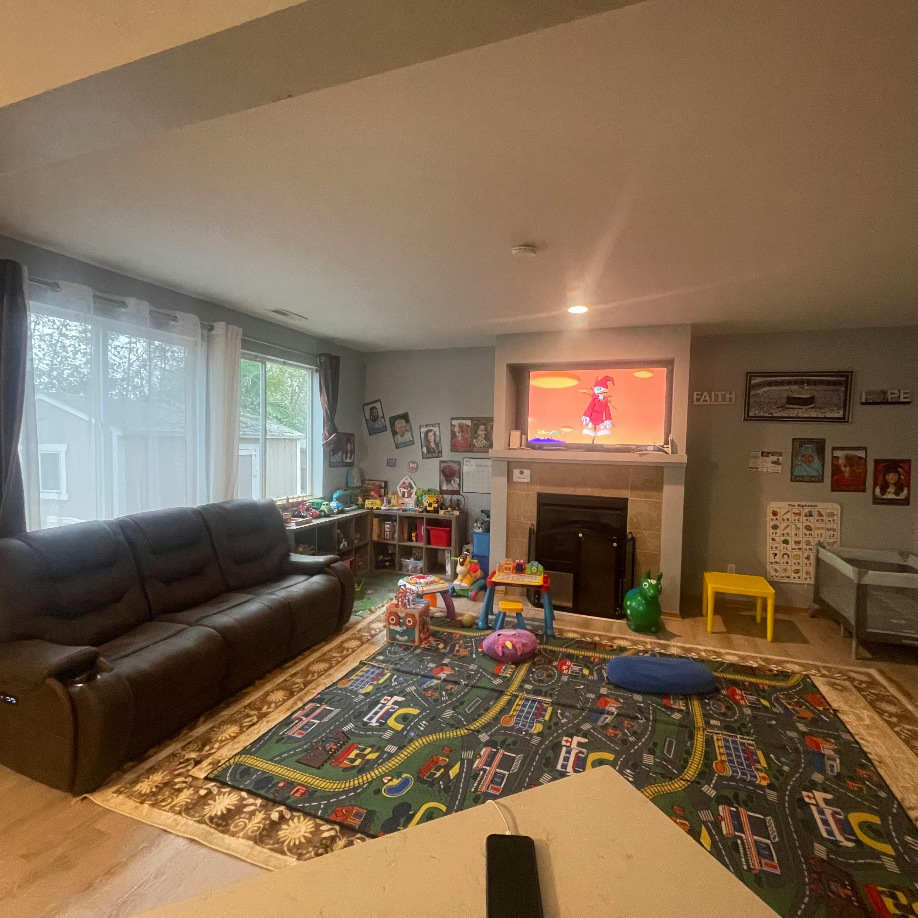 Living room with a large sofa, play rug, and television above-fireplace TV