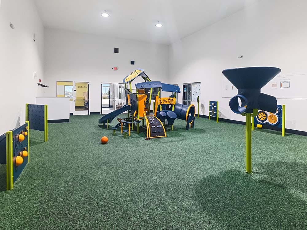 Indoor playground with blue and orange climbing structures on green turf
