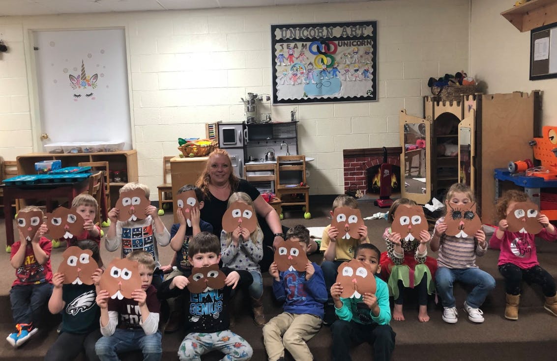 Adult and children holding up paper crafts in a classroom