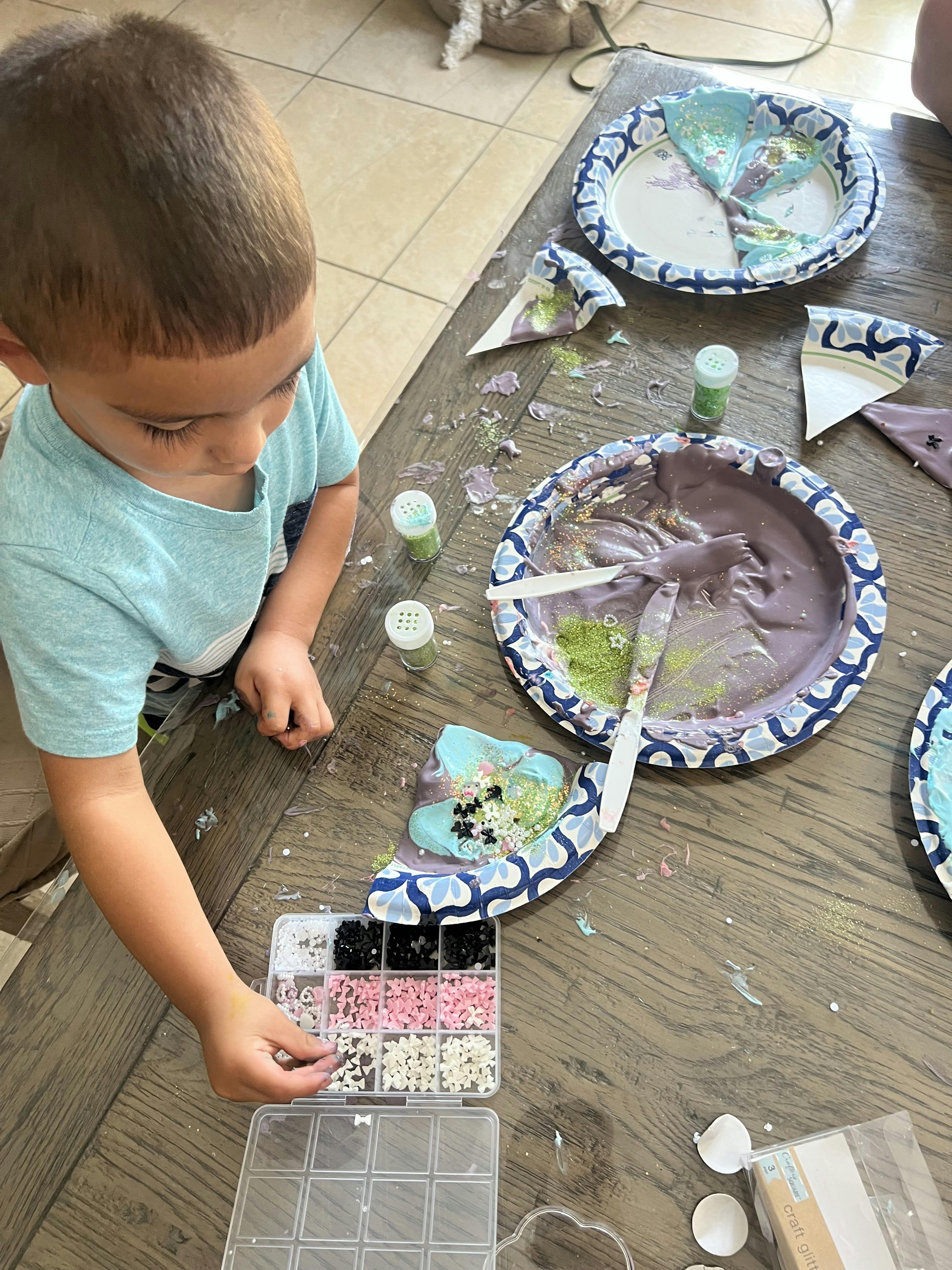Child crafting with glitter and small plastic shapes on paper plates