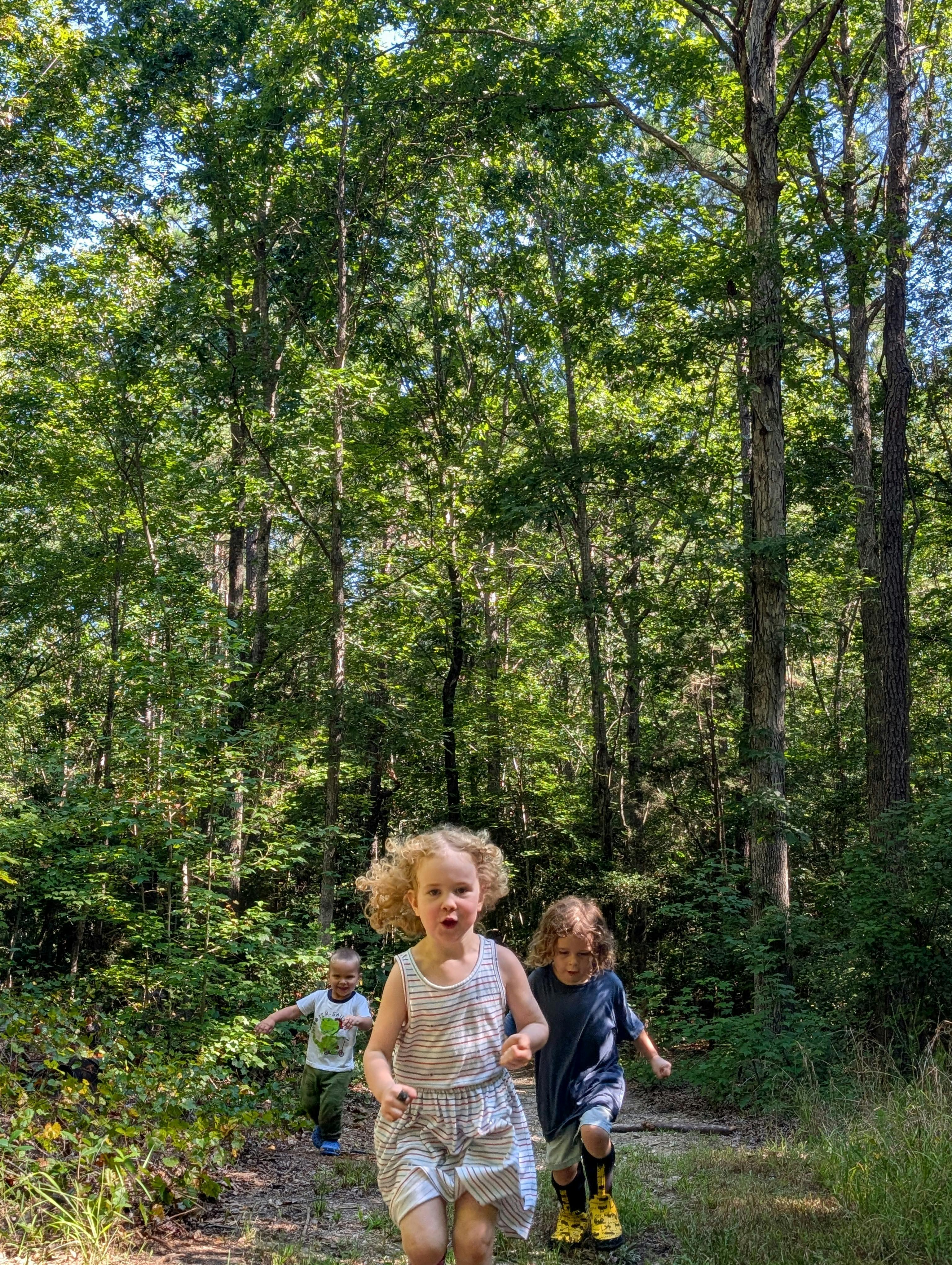 Three children running on a forest path
