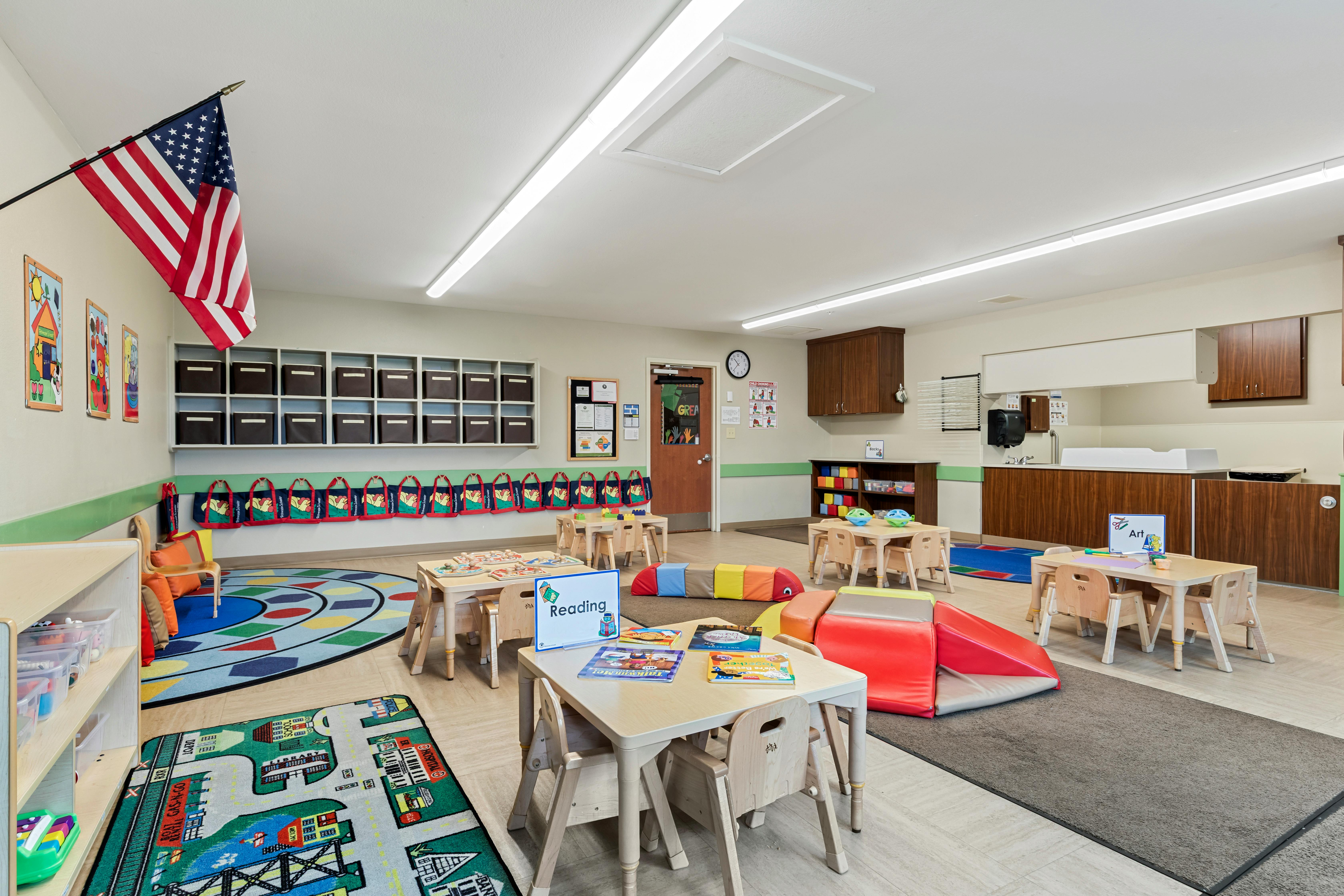 Classroom with small tables, chairs, colorful rugs, and play equipment