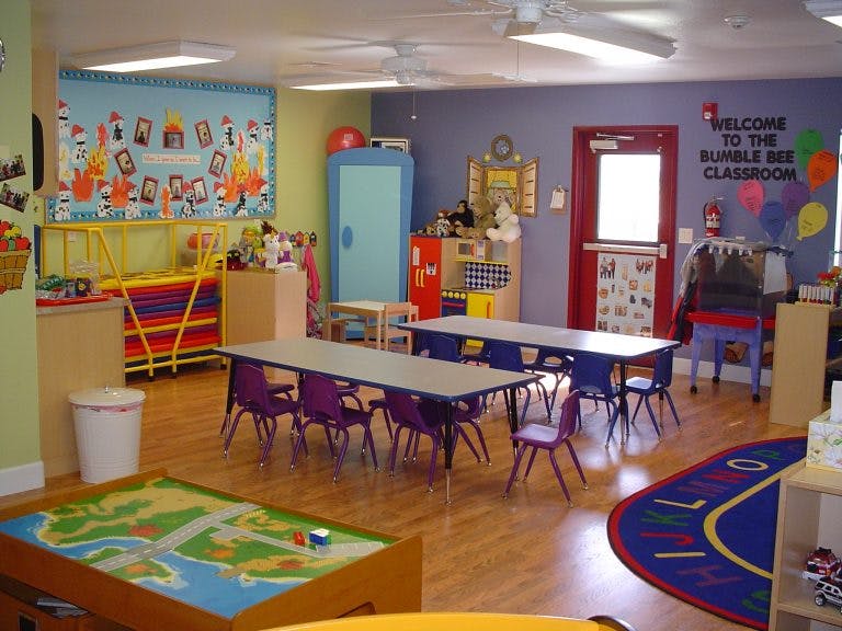Classroom with tables and chairs, play rug, and wall decorations