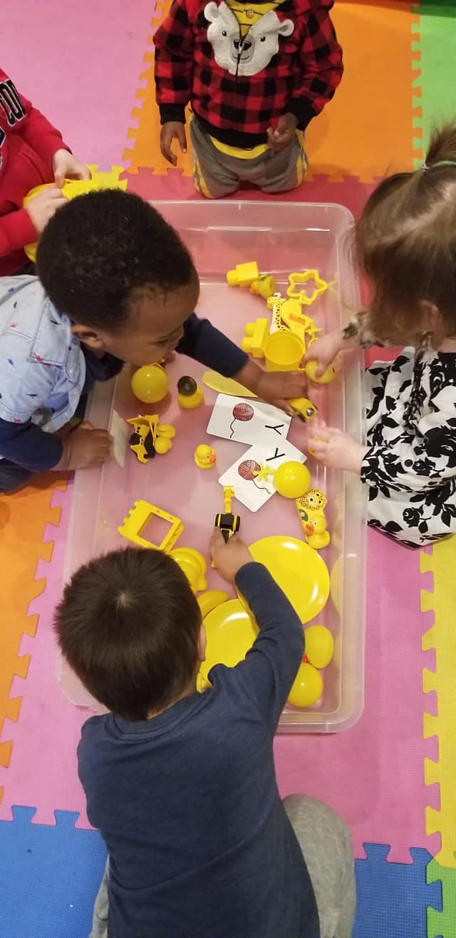Children playing with yellow toys in a clear bin
