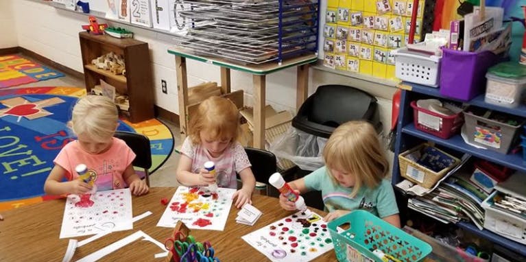 Three children doing crafts at a table in a classroom