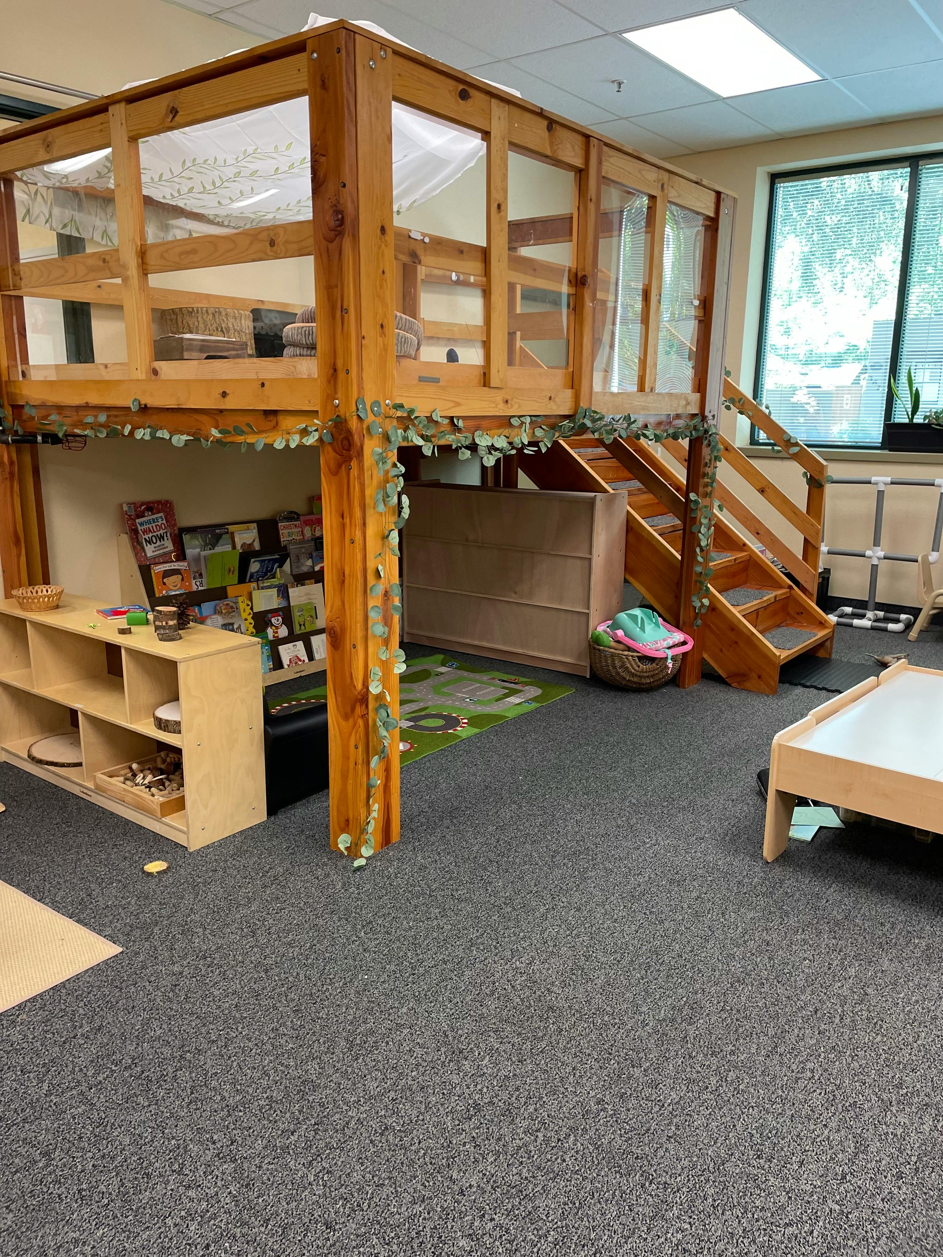 Indoor wooden play structure with stairs and a small bookshelf underneath area underneath