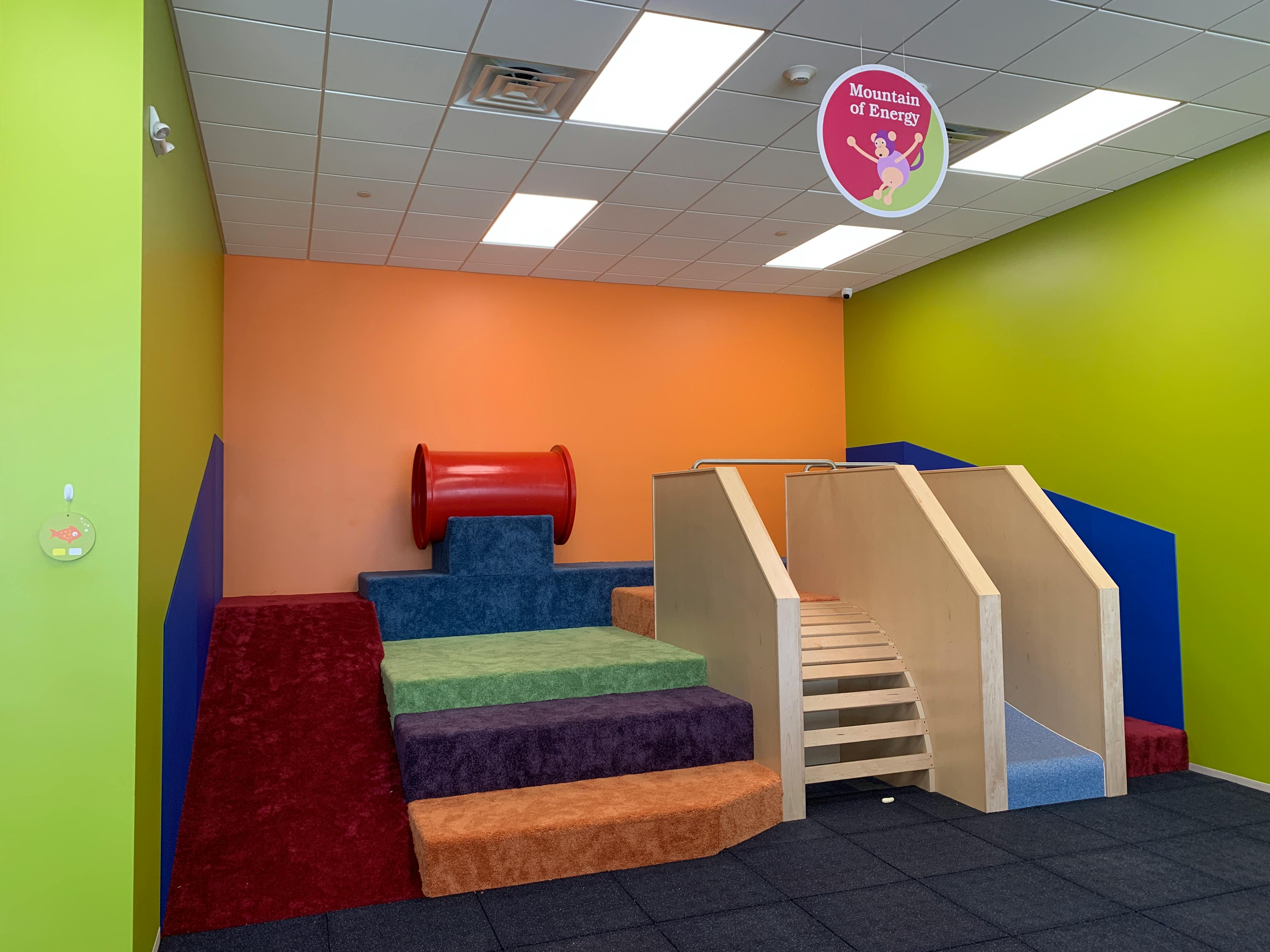 Indoor play area with soft steps, a red tunnel, and a wooden slide structure